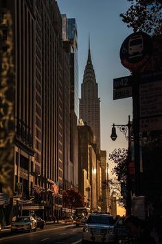 a city street with tall buildings on both sides and cars driving down the road at dusk