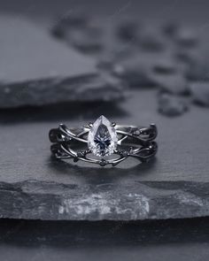 a white gold ring with a pear shaped diamond in the center on top of a rock