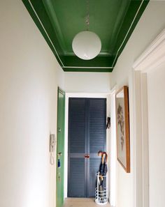 an empty hallway with green painted ceiling and white walls, two umbrellas hanging on the door