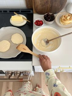 a person cooking pancakes in a pan on the stove with other food ingredients around them