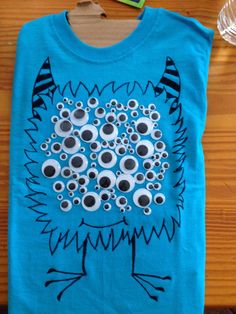 a blue t - shirt with an image of a monster made out of googly eyes