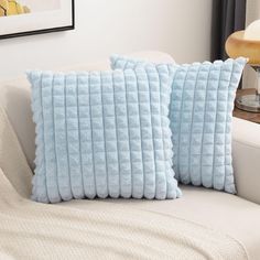 two blue pillows sitting on top of a white couch