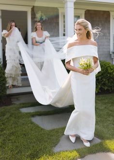 the bride is walking down the sidewalk with her veil blowing in the wind behind her