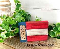 a wooden block with the word usa painted on it sitting next to some green plants