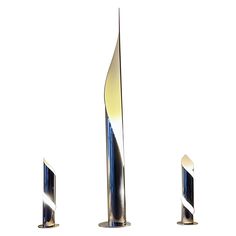 three tall metal sculptures sitting next to each other on a white surface with one standing in the middle