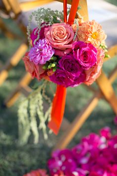 an orange ribbon tied to a chair with pink and red flowers hanging from it's back