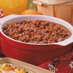 baked beans in a red casserole dish on a table next to oranges