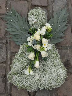 a bouquet of white roses and baby's breath sits on a brick surface in front of a stone wall