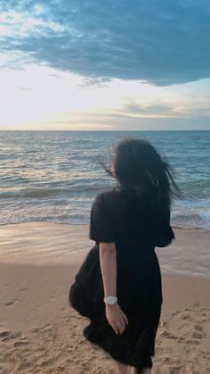 a woman is walking on the beach with her hair blowing in the wind as the sun sets