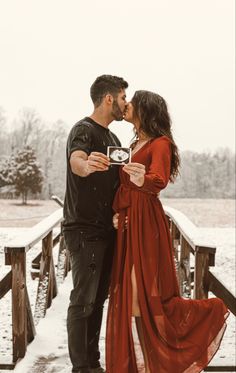 a man and woman are kissing on a bridge in the snow while holding an engagement ring