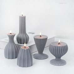 four candles are sitting next to each other on a white table with two vases and one candle holder