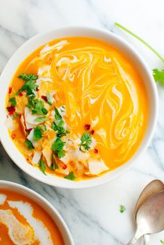 two bowls filled with soup and garnished with parsley next to spoons