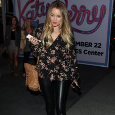 a woman in black leather pants holding a cell phone and standing next to a sign