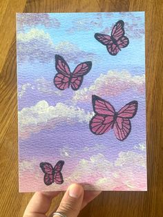 a hand holding up a piece of paper with pink butterflies on it and clouds in the background