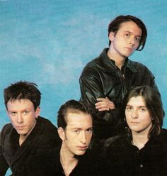 four men are posing for a photo in front of a blue background and one is wearing a black leather jacket