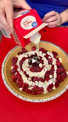 a person pouring cream on top of a cake with raspberries in the middle