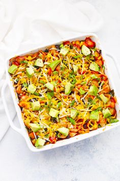 a casserole dish filled with vegetables and cheese on a white tablecloth next to a fork