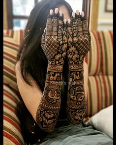 a woman sitting on top of a couch holding her hands up to her face with hendi