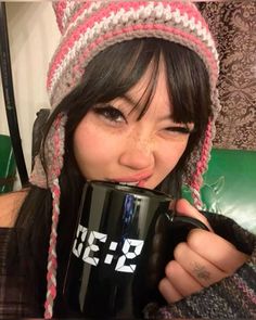 a woman wearing a knitted hat drinking from a coffee mug with her mouth open