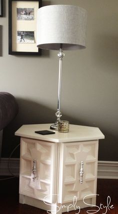 a lamp on top of a white cabinet in front of a wall with pictures above it