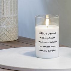 a candle with a poem on it sitting on a table next to a vase and potted plant