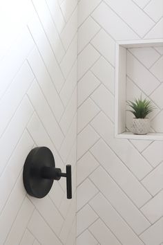 a white tiled bathroom with black fixtures and a potted plant in the window sill