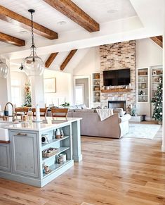 a large open concept kitchen and living room with wood flooring, white walls and beams