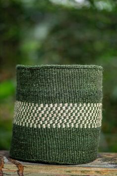 a green and white basket sitting on top of a wooden table in front of trees