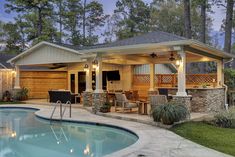 a backyard with a swimming pool and covered patio area at night, surrounded by trees