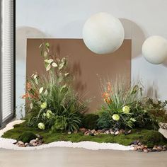 an arrangement of plants and rocks in front of a wall with balls hanging from it