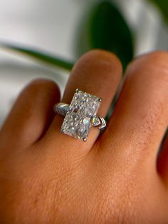 a woman's hand with a diamond ring on top of her finger and a green plant in the background