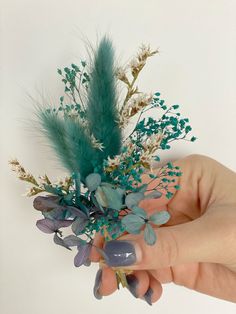 a hand holding a fake flower arrangement with blue and green flowers in it's center