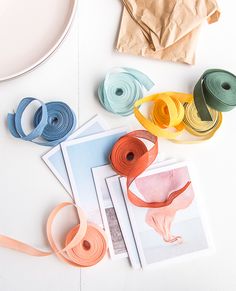 several different colored ribbons are laid out on a white surface next to some crafting supplies