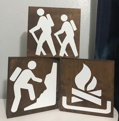 three wooden signs with white stickers depicting hikers and fire hydrants on them