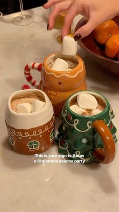 two mugs with marshmallows in them on a table next to oranges