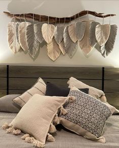 a bed topped with lots of pillows next to a wooden headboard covered in feathers