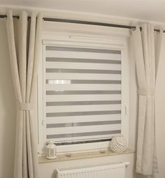 a white window with grey and white striped blinds on the windowsill, next to a radiator