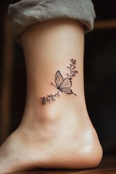 a small butterfly tattoo on the side of a woman's foot with flowers and leaves