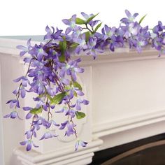 purple flowers are hanging from the top of a fireplace mantel