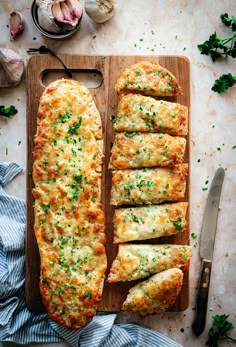 an overhead view of bread with cheese and herbs on a cutting board next to garlic