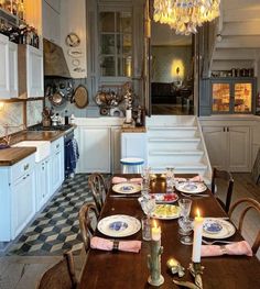 a dining room table is set with place settings and candles in front of the chandelier