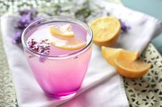 a glass filled with purple liquid next to sliced oranges and lavender sprigs