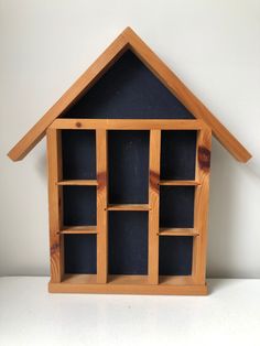 a wooden house shaped shelf with bookshelves and shelves on each side, against a white wall