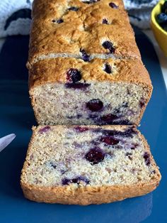 a loaf of blueberry bread sitting on top of a table next to a bowl of fruit