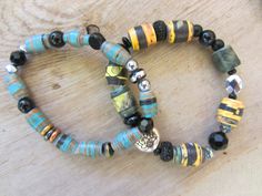 two bracelets made out of glass beads on a wooden table with a silver bead