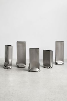 four silver vases sitting on top of a cement floor