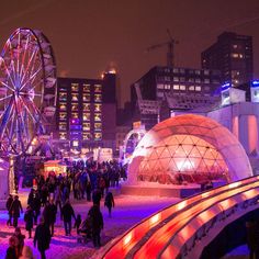 many people are walking around in the city at night with ferris wheel and buildings behind them