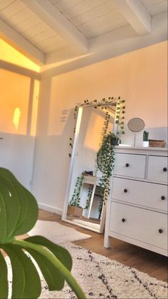 a room with a dresser, mirror and plant on the floor in front of it