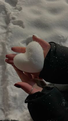 a woman's hand holding a white heart shaped snowball in the middle of some snow