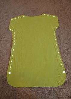 a yellow shirt with white stitching on the front and back, sitting on top of carpet